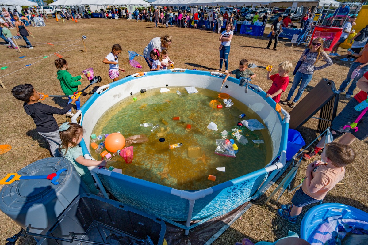Children use nets and grabber tools to pull plastic trash out of a pool of murky water at an interactive pollution activity at the Waterways Festival.
